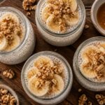 Four jars of brown butter banana bread protein chia cups topped with sliced bananas and walnuts on a wooden table