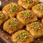 Golden pistachio kunafa cottage cheese toast bites on a white plate, drizzled with syrup and topped with chopped pistachios