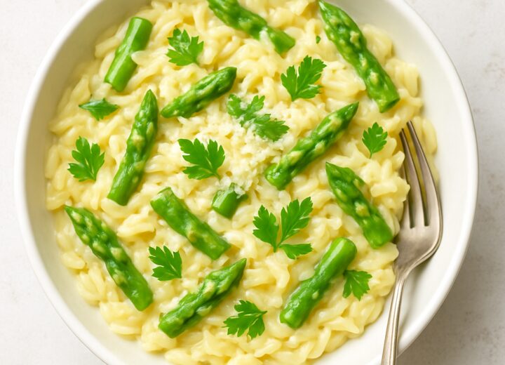 A bowl of creamy lemon parmesan asparagus orzo garnished with fresh parsley and Parmesan cheese