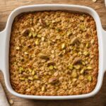 Brown butter pistachio oat latte baked oats in a white baking dish, topped with chopped pistachios and a golden brown crust.