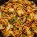 Crispy chili crisp cabbage noodle skillet in a cast iron pan, garnished with green onions and sesame seeds