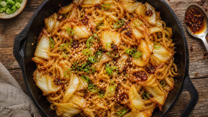 Crispy chili crisp cabbage noodle skillet in a cast iron pan, garnished with green onions and sesame seeds