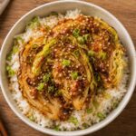 Crispy miso butter cabbage slices over steamed rice garnished with green onions and sesame seeds in a bowl