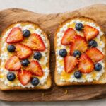 Yuzu honey cottage cheese fruit toast on a wooden board with strawberries and blueberries