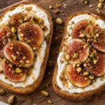Brown butter fig pistachio yogurt toast on a wooden board with sliced figs and chopped pistachios on sourdough bread