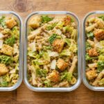Crunchy Caesar Lentil Pasta Salad Cups in meal prep containers with romaine lettuce and croutons
