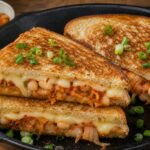 Kimchi white bean grilled cheese skillet sandwich with melted cheese and green onion garnish on a wooden board