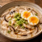 A bowl of miso mushroom chicken congee topped with green onions and sesame oil, with a spoon on the side.