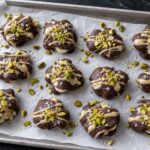 Pistachio Tahini Frozen Banana Clusters on a parchment-lined baking sheet, topped with chopped pistachios and sea salt.