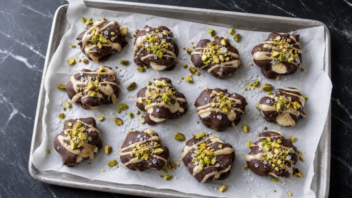 Pistachio Tahini Frozen Banana Clusters on a parchment-lined baking sheet, topped with chopped pistachios and sea salt.