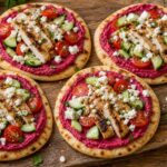 Roasted beet hummus chicken flatbreads with fresh veggies and feta on a wooden board.
