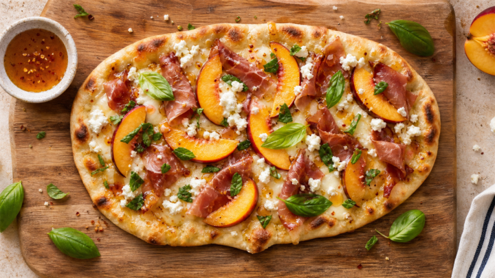 Crispy peach prosciutto flatbread with hot honey on a wooden board, garnished with fresh basil