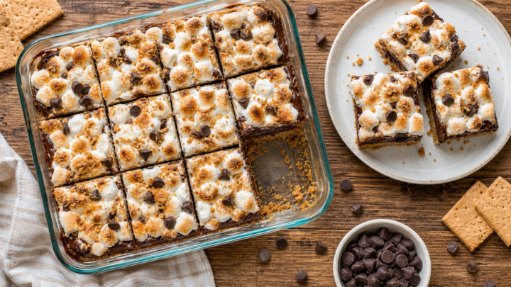 No-bake s'mores icebox bars on a white plate, showing layers of graham cracker crust, chocolate pudding, and marshmallows.