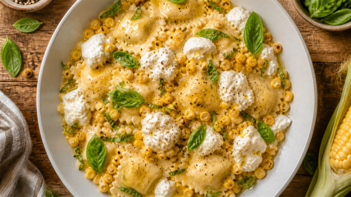 Bowl of summer corn and burrata ravioli topped with fresh basil, showcasing creamy cheese and golden corn kernels.