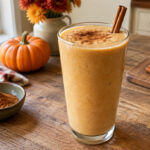 A creamy pumpkin spice protein smoothie in a glass with a cinnamon stick garnish.